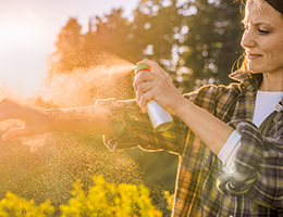 A woman sprays bug spray on her arm.