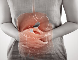 A woman's hands folded against her abdomen with a drawing of the digestive system superimposed.