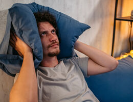 An annoyed man holds a pillow over his ears.