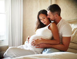 A man embraces a pregnant woman seated on a bed