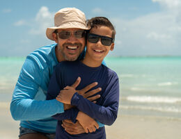 A father and son smile on a beach.