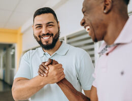 Two smiling men clasp hands.
