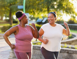 Two women smile at each other as they walk for exercise.