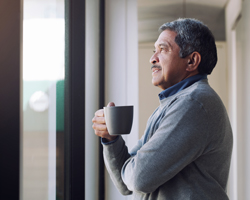 A man holds a mug and looks out a window.