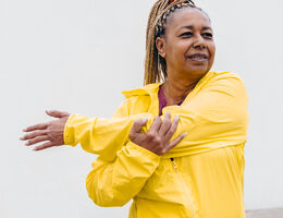 An older Black woman stretches her arm.