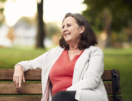 A woman sits on a park bench smiling.