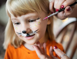 A young girl's face being painted with whiskers and freckles.
