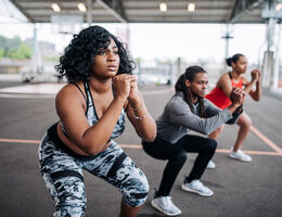 A row of people do squats on an outdoor basketball court.