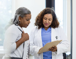 A doctor shows a patient her clipboard.