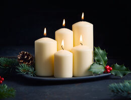 Five lighted candles of different heights on a plate with holly, pine sprigs and pine cones.