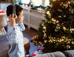 A young boy wearing pajamas and headphones looks at a Christmas tree.