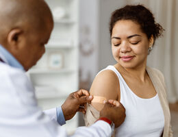A doctor puts an adhesive bandage on a woman’s upper arm.